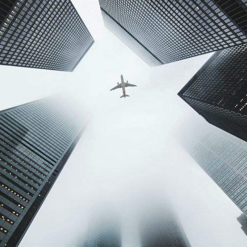 Airplane soaring above fog-enshrouded skyscrapers in an urban setting.
