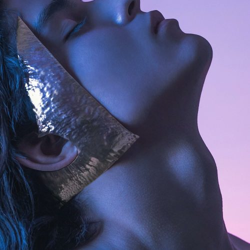 Creative portrait featuring a person with a metallic square element against a vibrant backdrop.