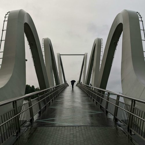 A solitary figure walks across an iconic modern bridge in Kyiv, Ukraine, against a moody sky.
