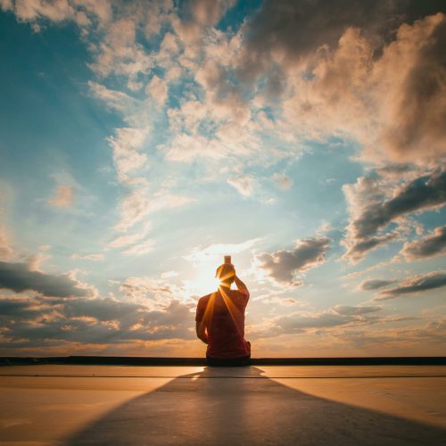 Silhouette of a figure meditating against a stunning sunset sky, creating a serene and peaceful atmosphere.