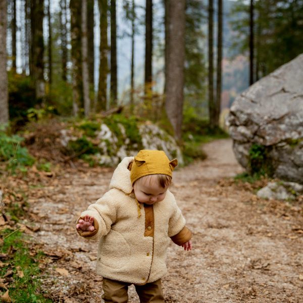 A cute baby in a bear hoodie walking on a forest trail during autumn.