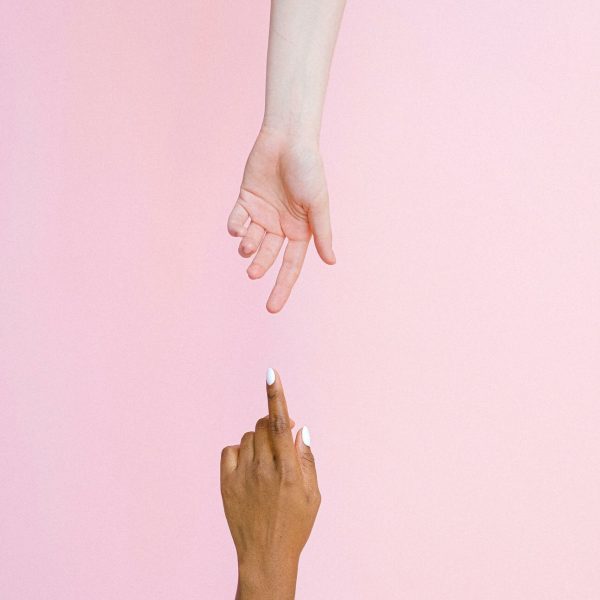 Two hands reaching towards each other on a light pink background, symbolizing connection and diversity.