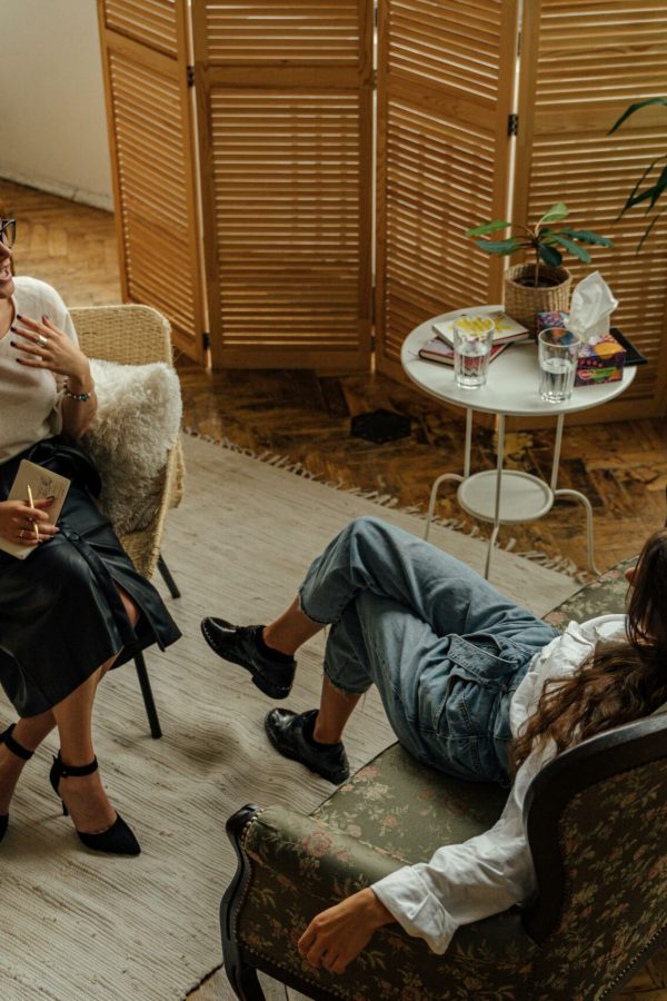 Two women engaged in a psychotherapy session in a warm, inviting interior with plants and natural lighting.