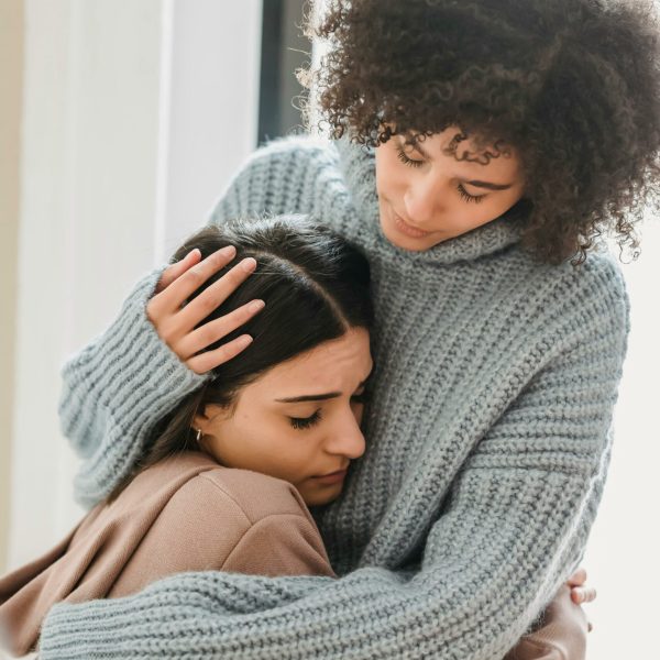 Young multiethnic female friends in casual clothes embracing each other while crying in light apartment