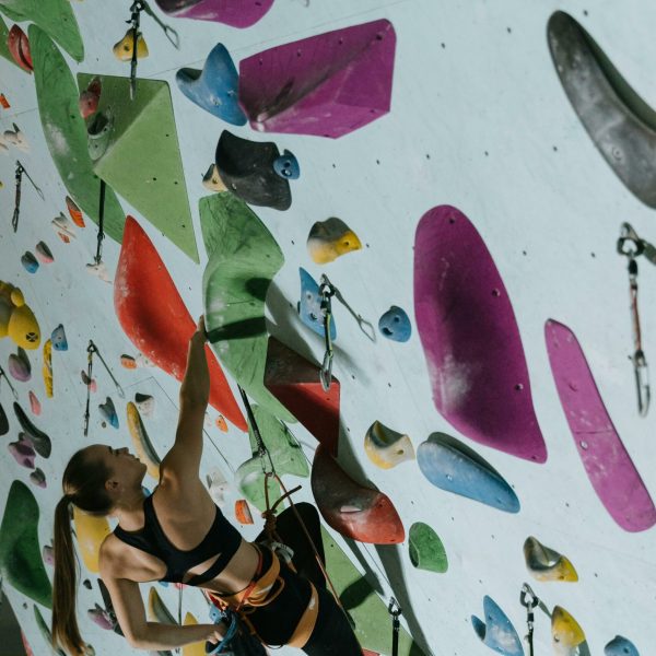 A woman practicing indoor rock climbing on a vibrant and colorful climbing wall.