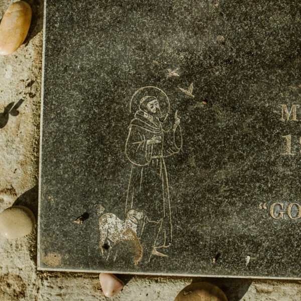A textured gravestone featuring a saint and adorned with pebbles, symbolizing remembrance and serenity.