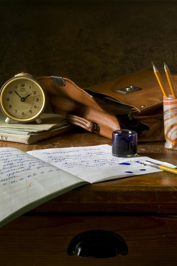 Classic wooden desk with writing materials, vintage clock, and a leather bag.